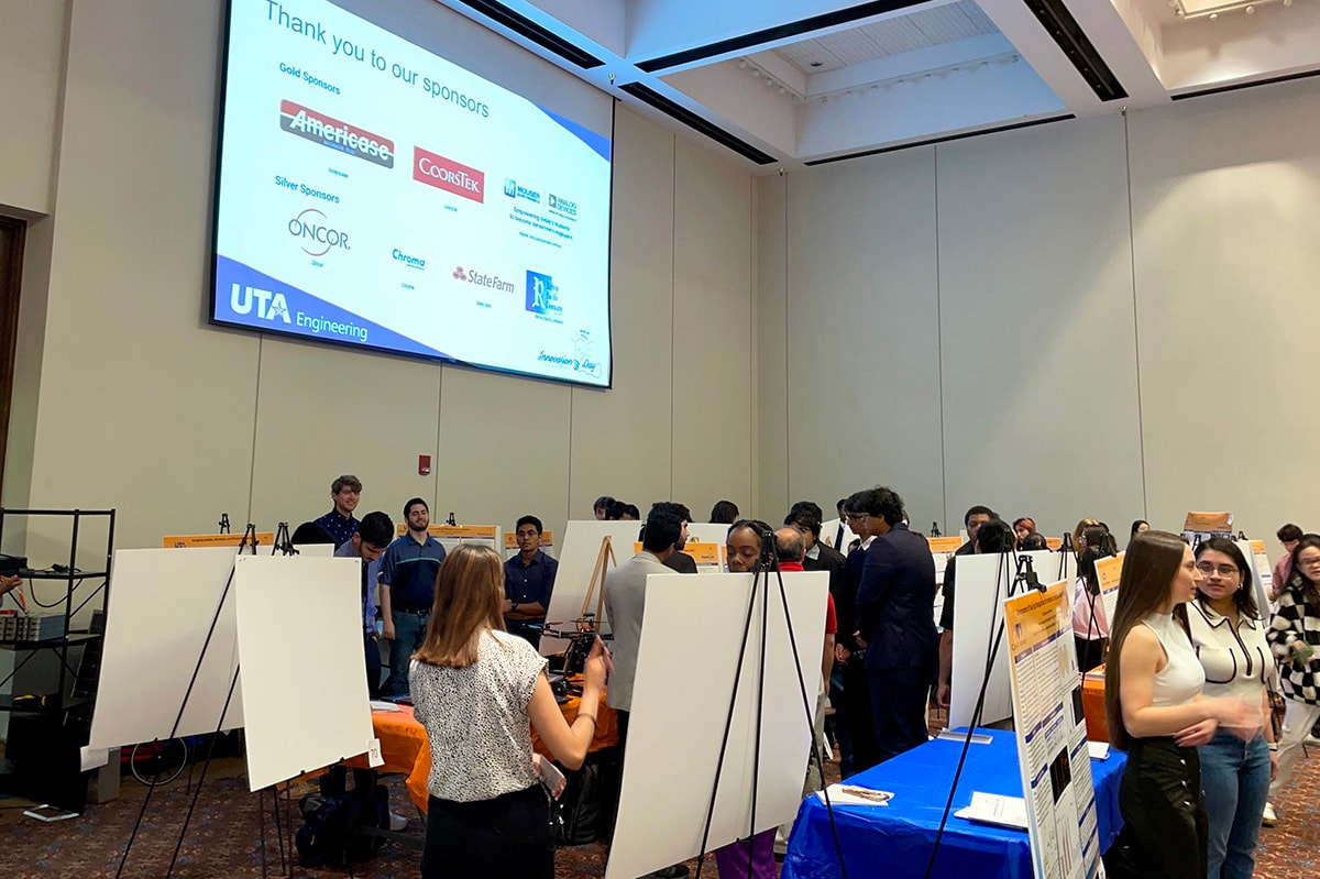 Several students standing by their projects in a large room at a UTA event - opens in a new tab