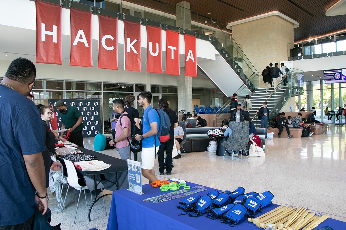 Students standing at booths at Hack UTA event - opens in a new tab